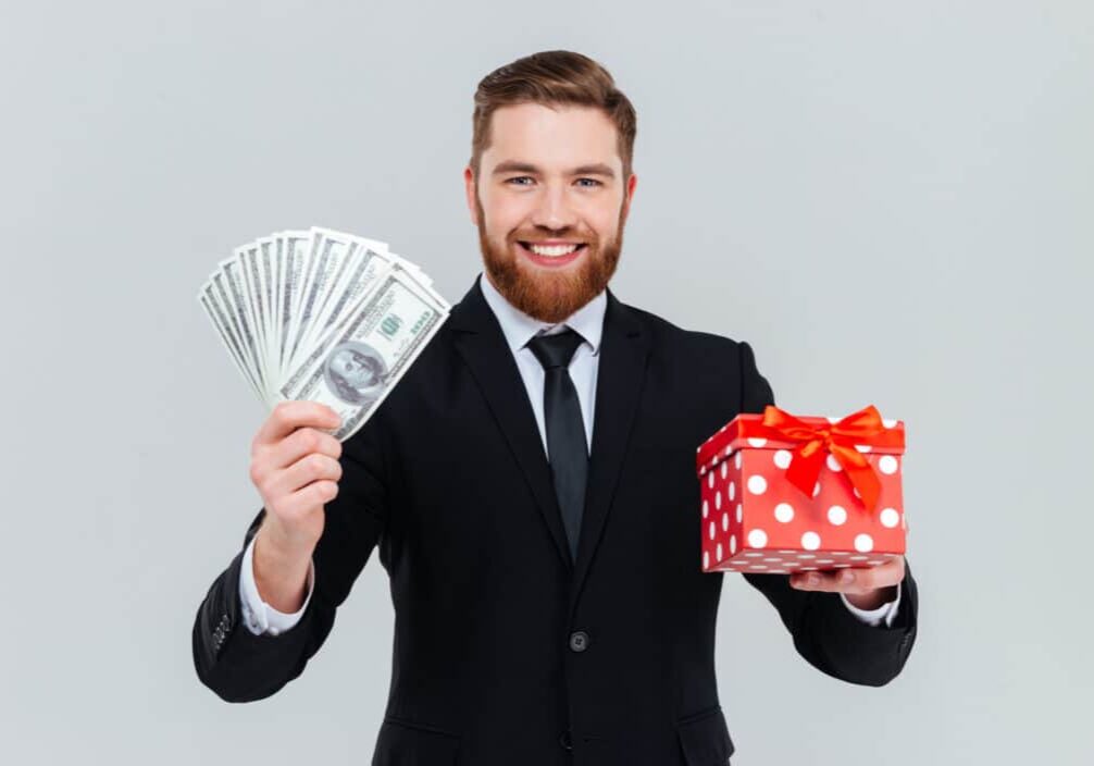 Happy handsome business man in suit holding gift and money in hands. Isolated gray background