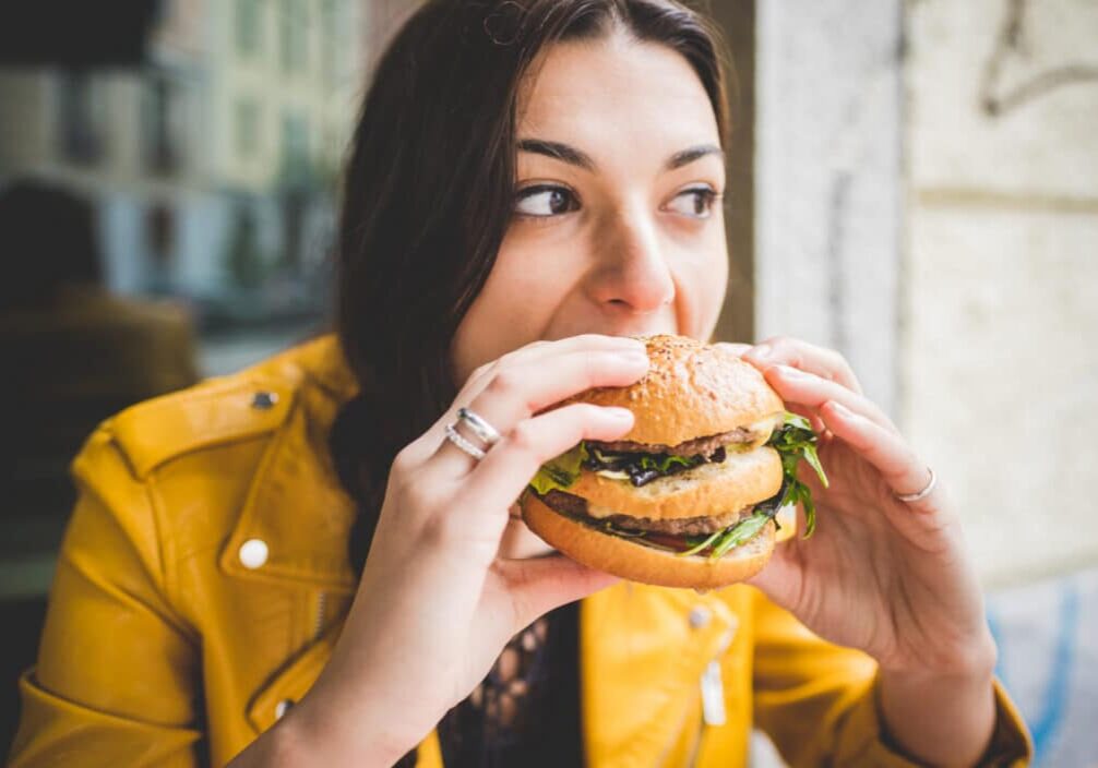Young woman sitting  eating an hamburger hand hold- hunger, food, meal concept